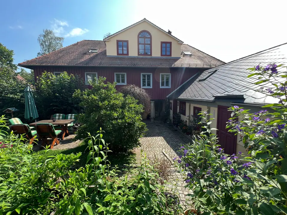 Das Retzschgut von der Gartenseite: Giebel mit Bogenfenster, ochsenblutrotes Obergeschoss, davor der Garten mit Sitzplatz